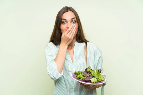 Young woman with salad over isolated green wall with surprise facial expression