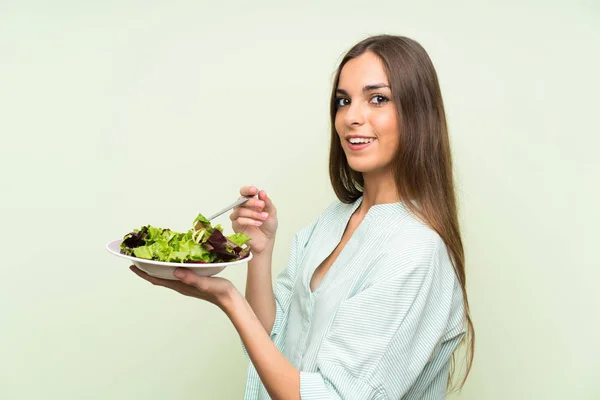 Young woman with salad over isolated green wall