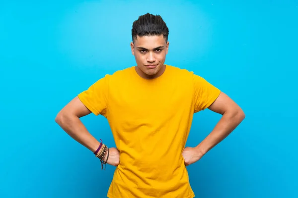 Young man with yellow shirt over isolated blue background angry