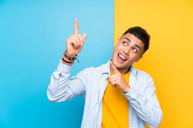 İşaret parmağı ile işaret izole renkli arka plan üzerinde Genç adam harika bir fikir