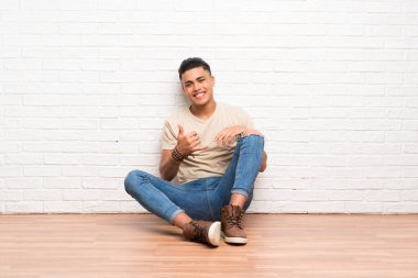 Yerde oturan ve telefon jesti yapan genç adam