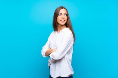 Kolları çapraz ve mutlu bir şekilde izole edilmiş mavi bir geçmişi olan genç bir kadın.