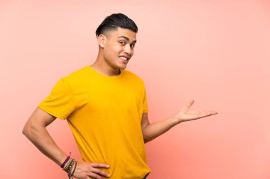 Izole pembe duvar üzerinde sarı gömlekli genç adam gelmeye davet için yan ellerini uzatıyor