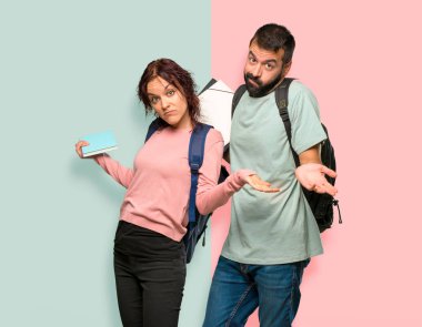 Renkli duvarda omuz kaldırırken sırt çantaları ve kitapları olan iki öğrenci şüphe jesti yapıyor