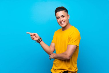 Izole mavi arka plan üzerinde sarı gömlek li genç adam yan parmak işaret