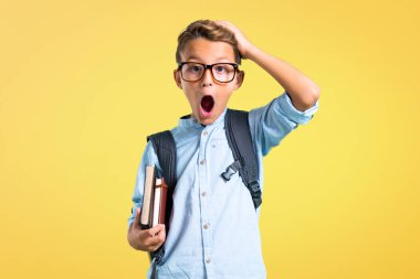 Sırt çantası ve gözlük ile Öğrenci çocuk mutsuz ve bir şey ile sinirli. Sarı arka planda negatif yüz ifadesi