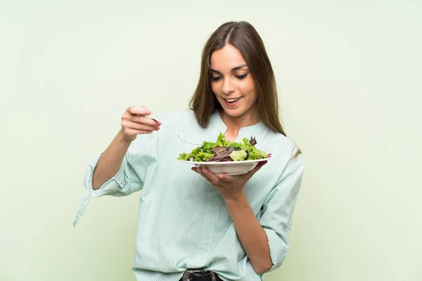Young woman with salad over isolated green wall