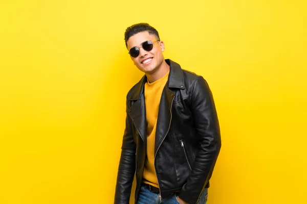 Young man over isolated yellow background with glasses and happy