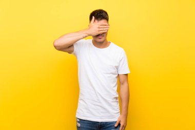 Gözleri elleriyle kaplayan izole sarı arka plan üzerinde genç yakışıklı adam. Bir şey görmek istemiyorum