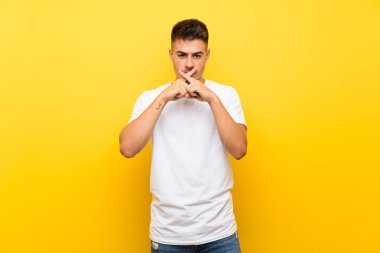 Soyutlanmış sarı arka planda genç yakışıklı bir adam sessizlik işareti gösteriyor.