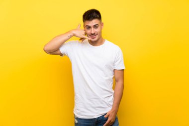 Izole sarı arka plan üzerinde telefon jest yapma genç yakışıklı adam. Beni geri arayın işareti