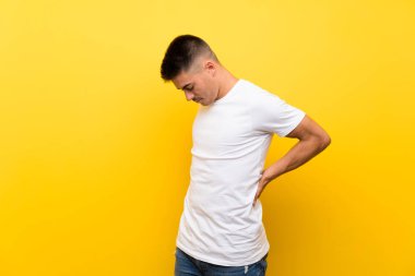 Bir çaba yapmış olduğu için sırt ağrısı muzdarip izole sarı arka plan üzerinde Genç yakışıklı adam