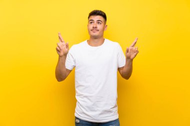 Genç yakışıklı, izole edilmiş sarı arka planda, şans diliyor ve en iyisini diliyor.