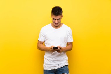 Izole sarı arka plan üzerinde genç yakışıklı adam cep ile bir mesaj gönderme