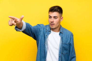 Izole sarı arka plan üzerinde genç yakışıklı adam uzağa işaret