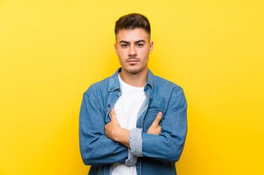 Izole sarı arka plan üzerinde genç yakışıklı adam kollarını çapraz tutmak