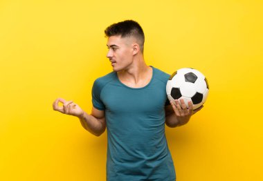 Yakışıklı genç futbolcu sürpriz yüz ifadesi ile izole sarı arka plan üzerinde