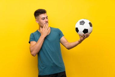 Yakışıklı genç futbolcu nun üzerinde izole edilmiş sarı arka plan ile sürpriz ve şok yüz ifadesi