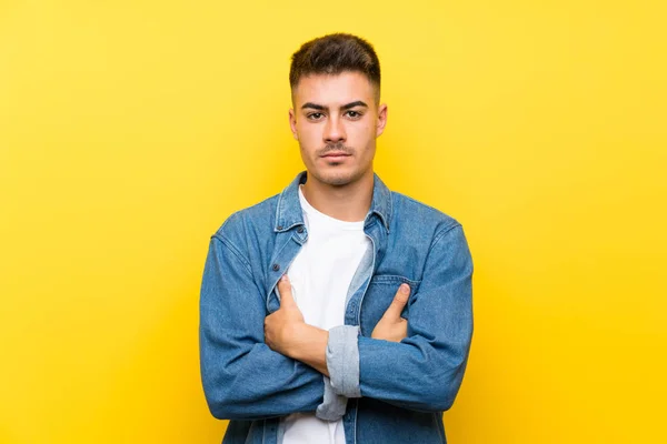Young handsome man over isolated yellow background keeping arms crossed