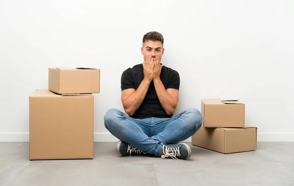Handsome young man moving in new home among boxes with surprise facial expression