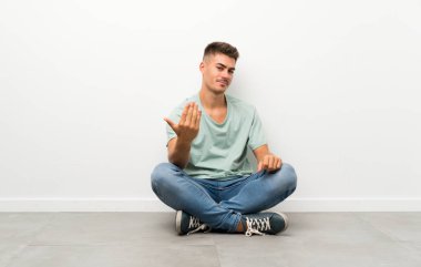 Genç yakışıklı adam yere oturmuş, davet ediyor.