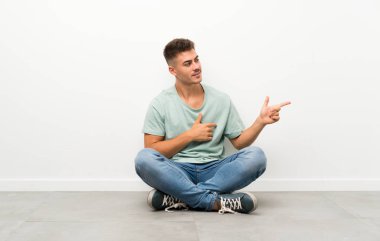 Genç yakışıklı adam yerde oturuyor ve parmağını yana doğru gösteriyor.