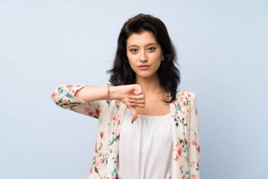 Izole mavi arka plan üzerinde genç kadın başparmak aşağı işareti gösteren