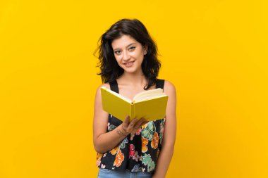 Izole sarı arka plan üzerinde genç kadın tutma ve bir kitap okuma