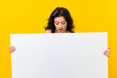 Bir kavram eklemek için boş beyaz bir pankart tutan izole sarı arka plan üzerinde genç kadın