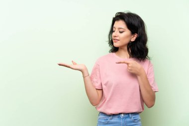 Bir reklam eklemek için avuç üzerinde copyspace hayali tutan izole yeşil arka plan üzerinde genç kadın