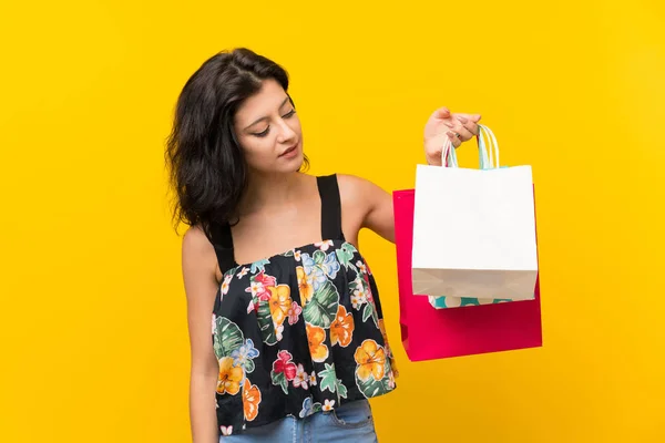 多くの買い物袋を持つ孤立した黄色の背景の上の若い女性 — ストック写真