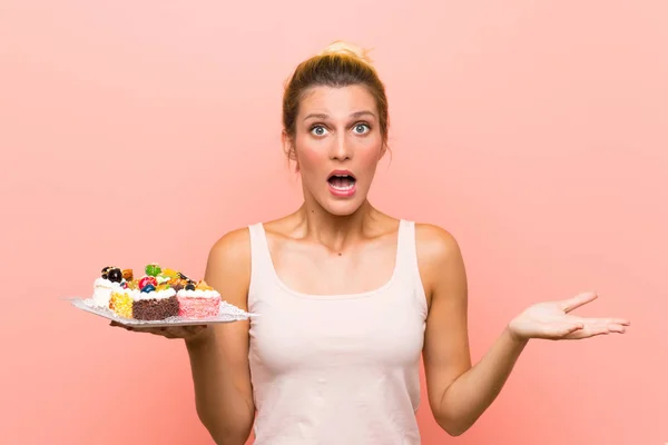 Junge Blonde Frau Hält Viele Verschiedene Mini Kuchen Mit Schockiertem — Stockfoto