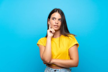 Izole mavi arka plan üzerinde genç kız bakarken bir fikir düşünme