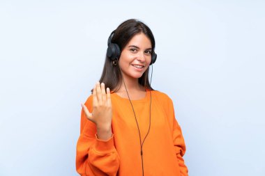 Genç kadın el ile gelmeye davet izole mavi duvar üzerinde bir cep ile müzik dinliyor. Geldiğin için mutluyum.