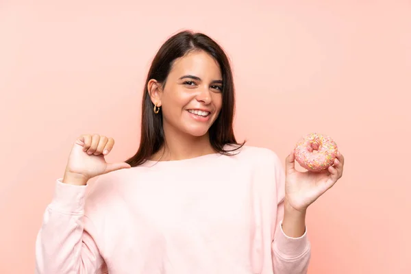 年轻女孩拿着一个甜甜圈在孤立的粉红色背景骄傲和自我满足 — 图库照片