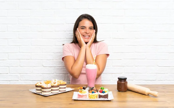 Junges Mädchen Mit Vielen Verschiedenen Mini Kuchen Mit Überraschendem Gesichtsausdruck — Stockfoto