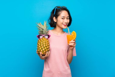 Güneş gözlüğü ile bir ananas tutan izole mavi arka plan üzerinde Asya genç kadın