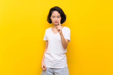 Asya genç kadın üzerinde izole sarı duvar sinirli ve işaret ön