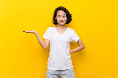 Asya genç kadın üzerinde izole sarı duvar tutan boşaltmak hayali Palm üzerinde bir reklam eklemek