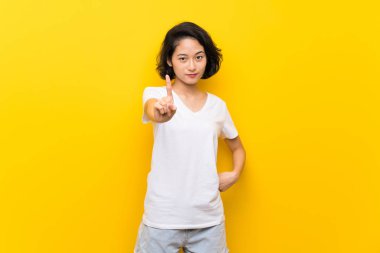 Asya genç kadın üzerinde izole sarı duvar gösteren ve kaldırma bir parmak