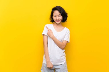 Bir ürün sunmak için yan işaret izole sarı duvar üzerinde Asya genç kadın