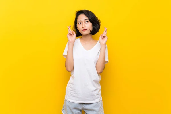 Asiática Joven Sobre Aislada Pared Amarilla Con Los Dedos Cruzando —  Fotos de Stock