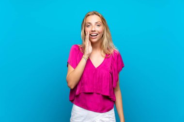 Sürpriz ve şok yüz ifadesi ile izole mavi arka plan üzerinde Sarışın genç kadın