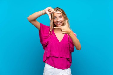 Izole mavi arka plan odaklama yüz üzerinde Sarışın genç kadın. Çerçeveleme simgesi