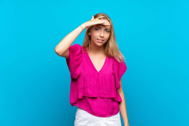Izole mavi arka plan üzerinde Sarışın genç kadın uzak el ile bir şey bakmak için bakıyor