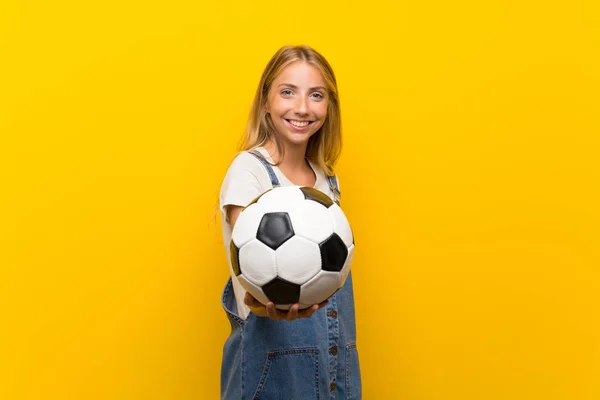 Blond Młoda Kobieta Białym Tle Żółty Trzymając Piłkę Nożną — Zdjęcie stockowe