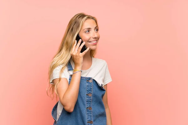 Joyeux Blonde jeune femme avec un téléphone mobile sur mur rose isolé — Photo