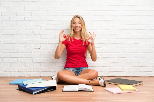 Joven Estudiante Rubia Con Muchos Libros Suelo Mostrando Signo Con — Foto de Stock