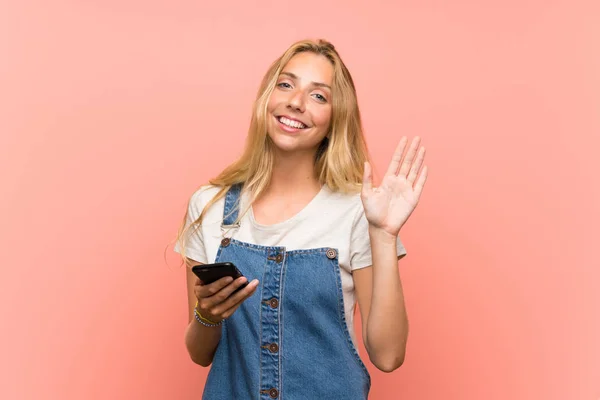 Jovem Loira Com Telefone Celular Sobre Parede Rosa Isolada Saudando — Fotografia de Stock