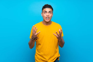 Izole mavi arka plan üzerinde sarı gömlek li genç adam kötü bir durum tarafından sinirli